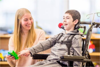 A special education aide helps a student in a wheelchair hold a building block